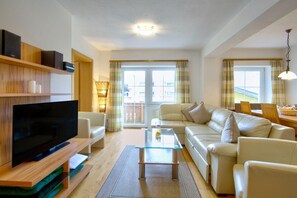 A modern living room with a flat-screen TV, a sofa, a coffee table, and a dining area with chairs. - Apartment in Wildschönau Vicky small apartment (Wildsch önau)