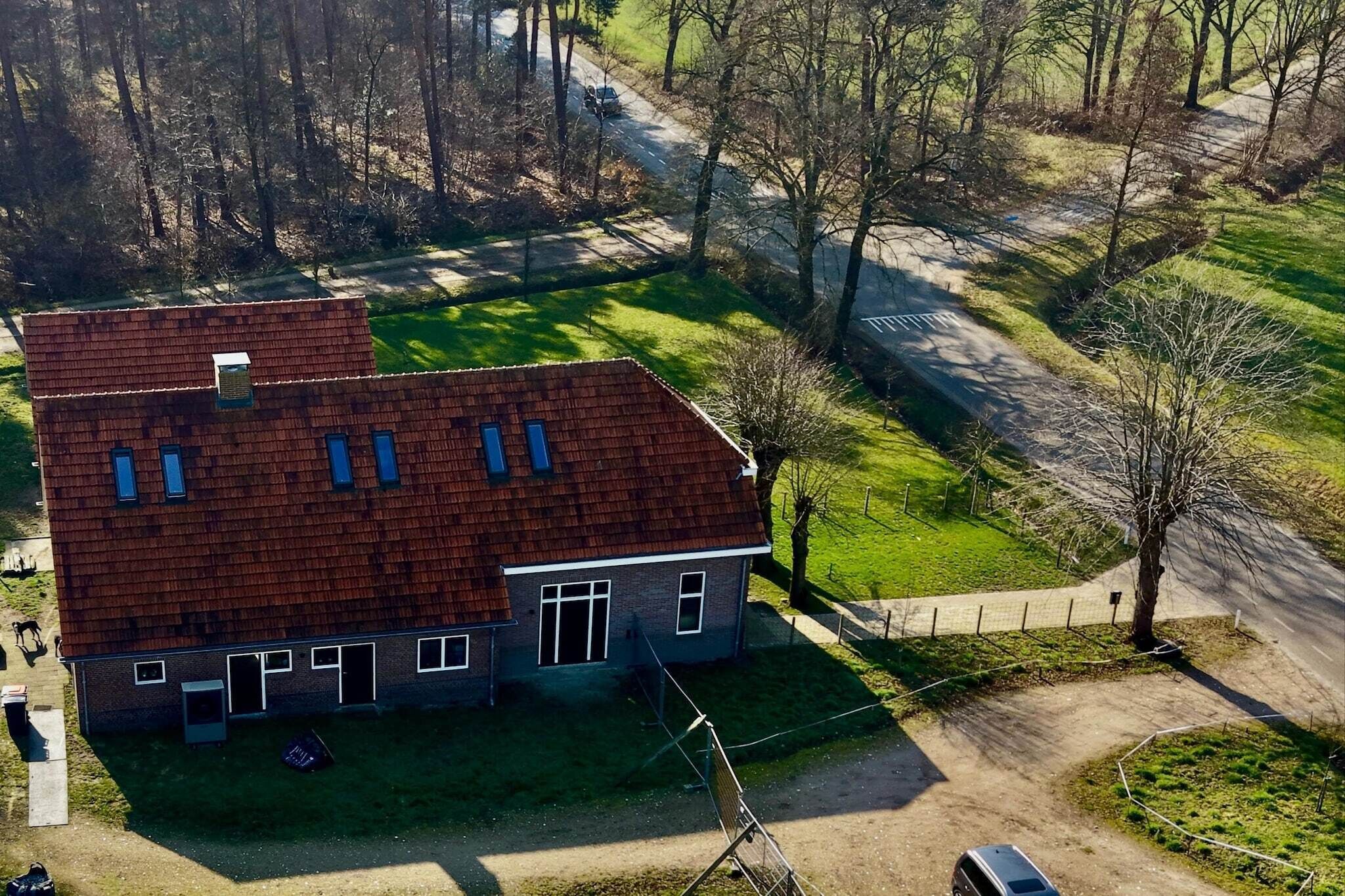 Kaksikerroksinen rakennus, jossa on punainen katto, aidattu piha ja asfaltoitu ajotie.
