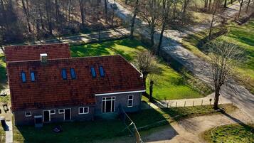 Kaksikerroksinen rakennus, jossa on punainen katto, aidattu piha ja asfaltoitu ajotie.