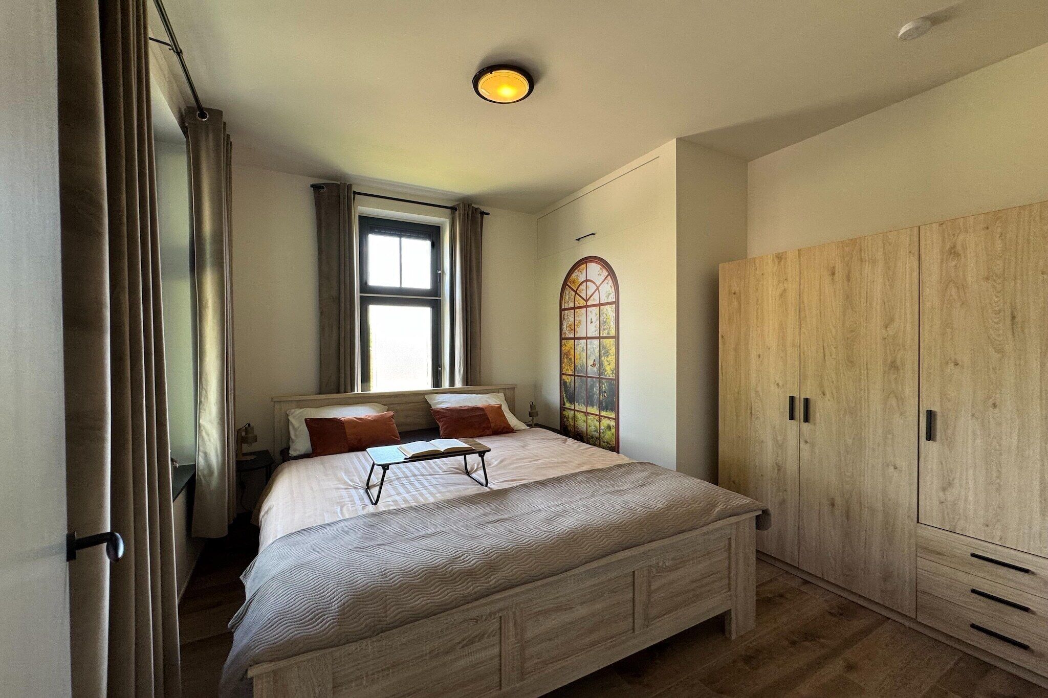 A bedroom with a bed, a window, a wardrobe, and a wall-mounted light fixture.