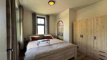 A bedroom with a bed, a window, a wardrobe, and a wall-mounted light fixture.