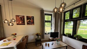 Un coin repas avec une table dressée pour deux personnes, un téléviseur et une fenêtre donnant sur un paysage verdoyant.