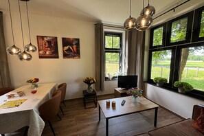 A dining area with a table set for two, a television, and a window with a view of greenery. - Langelshoes Guesthouse (Haaksbergen)