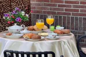 A table set for breakfast with croissants, a teapot, cups, and a vase of flowers. - Langelshoes Guesthouse (Haaksbergen)