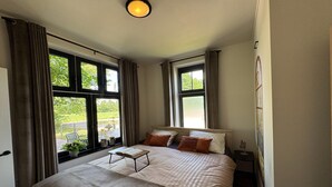 Une chambre à coucher avec un lit, une table de chevet, une fenêtre avec des rideaux et une vue sur la verdure à l’extérieur.