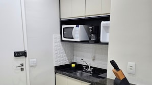 Cozinha com bancada de granito preto, porta branca e micro-ondas sobre a pia.