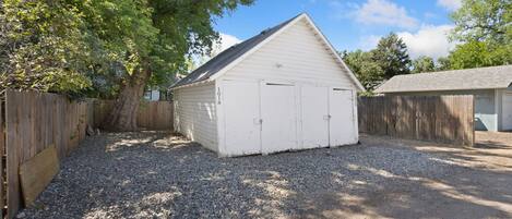 A white single-story building with a gabled roof, surrounded by a wooden fence and gravel driveway.