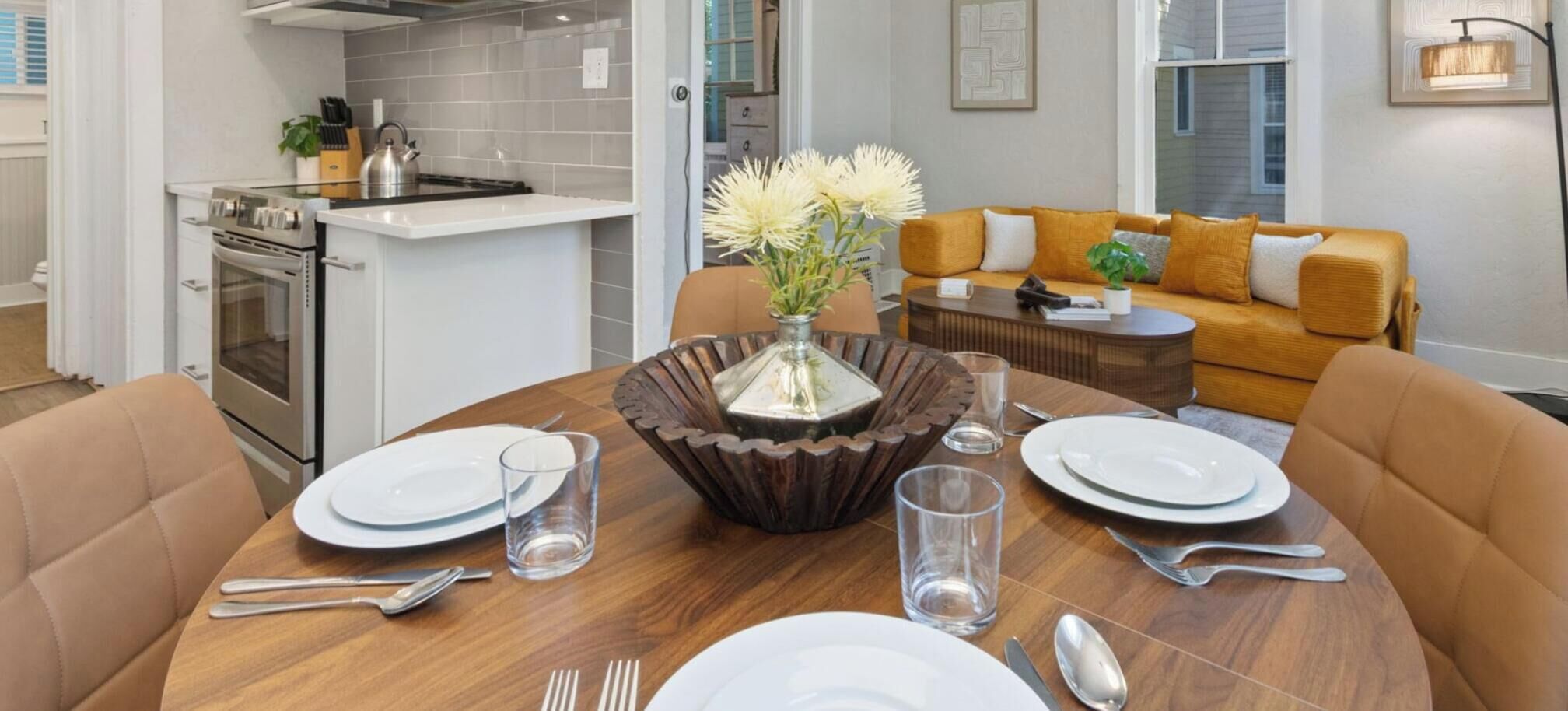 A dining table set with plates, cutlery, and glasses, surrounded by a brown table runner and a decorative vase.