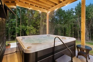 Ein Whirlpool in einer Außenanlage mit einer hölzernen Pergola darüber und bewaldeter Umgebung.