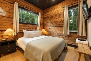 Ein Schlafzimmer mit einer Wand aus Holzbalken, einem Bett mit weißer Bettwäsche, zwei Nachttischlampen und einem Fenster mit Vorhängen.