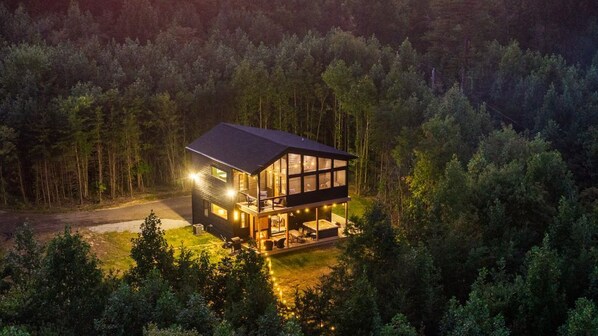 Eine zweistöckige Holzhütte mit einem Balkon, umgeben von einem Wald.
