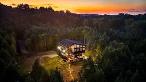 A modern house with a large glass facade, surrounded by dense forest, and a visible driveway leading to the entrance. - Escape to Nature's Wonderland: The rolling  foothills of Appalachia (Logan)