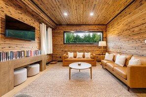 A cozy living room with a wooden ceiling, a large window, a sofa set, a coffee table, and a bookshelf. - Escape to Nature's Wonderland: The rolling  foothills of Appalachia (Logan)