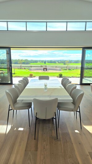 Een moderne eetruimte met een grote tafel en stoelen, grote ramen met uitzicht op een groen landschap.