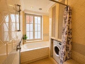 Ein Badezimmer mit einer Badewanne, einer Waschmaschine und einem Fenster mit satinierten Scheiben.