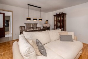 A living room with a beige sofa, a dining table with chairs, and a wooden cabinet. - Nice home in Grižane-Belgrad with garden (Grižane-Belgrad)