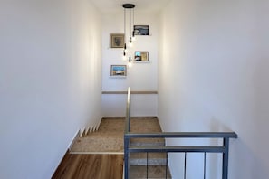 A staircase with a wooden floor and a metal railing, leading to a landing with wall-mounted artwork. - Nice home in Grižane-Belgrad with garden (Grižane-Belgrad)
