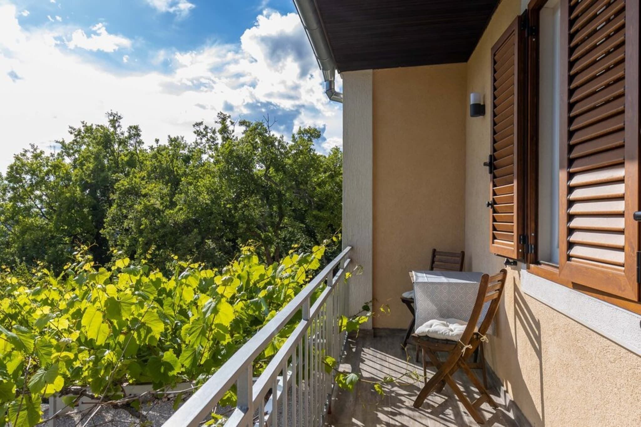 Ein Balkon mit Stuhl und Tisch, mit Blick auf einen Garten voller Grün.