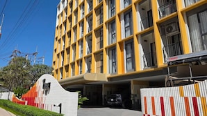 Un hotel de diversos pisos amb façana groga, balcons i una zona d'aparcament.