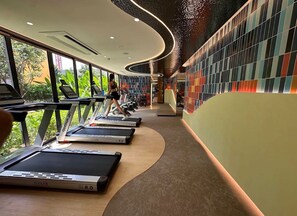 Un gimnasio con cintas de correr, una persona ejercitándose y una pared con baldosas de colores.