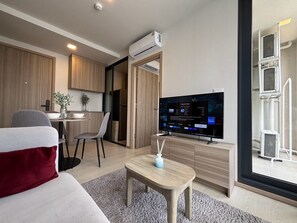A modern living room with a flat-screen TV, a dining area, and a kitchen. - 2-bed at The Base Rise, Near Central Phuket (Wichit)