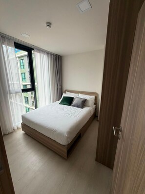 Un dormitorio moderno con una cama grande, una ventana con cortinas y vistas a edificios.