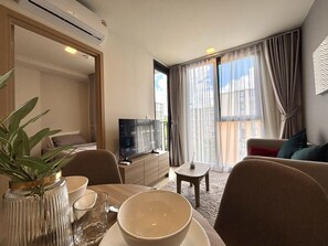 Habitación de hotel con comedor, televisión, sofá y un amplio ventanal con cortinas.