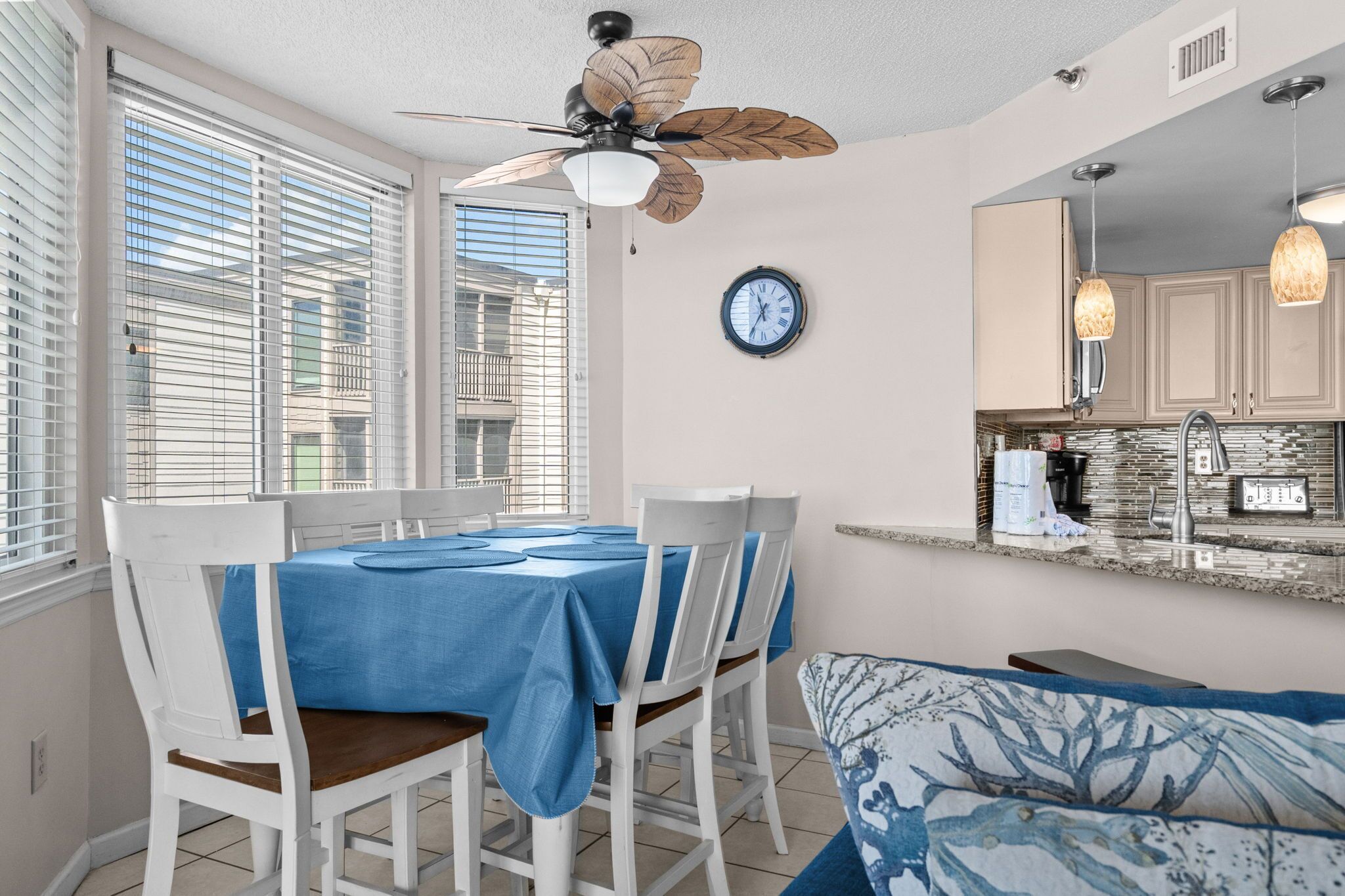 A compact kitchen with a dining area, a ceiling fan, and a clock on the wall.