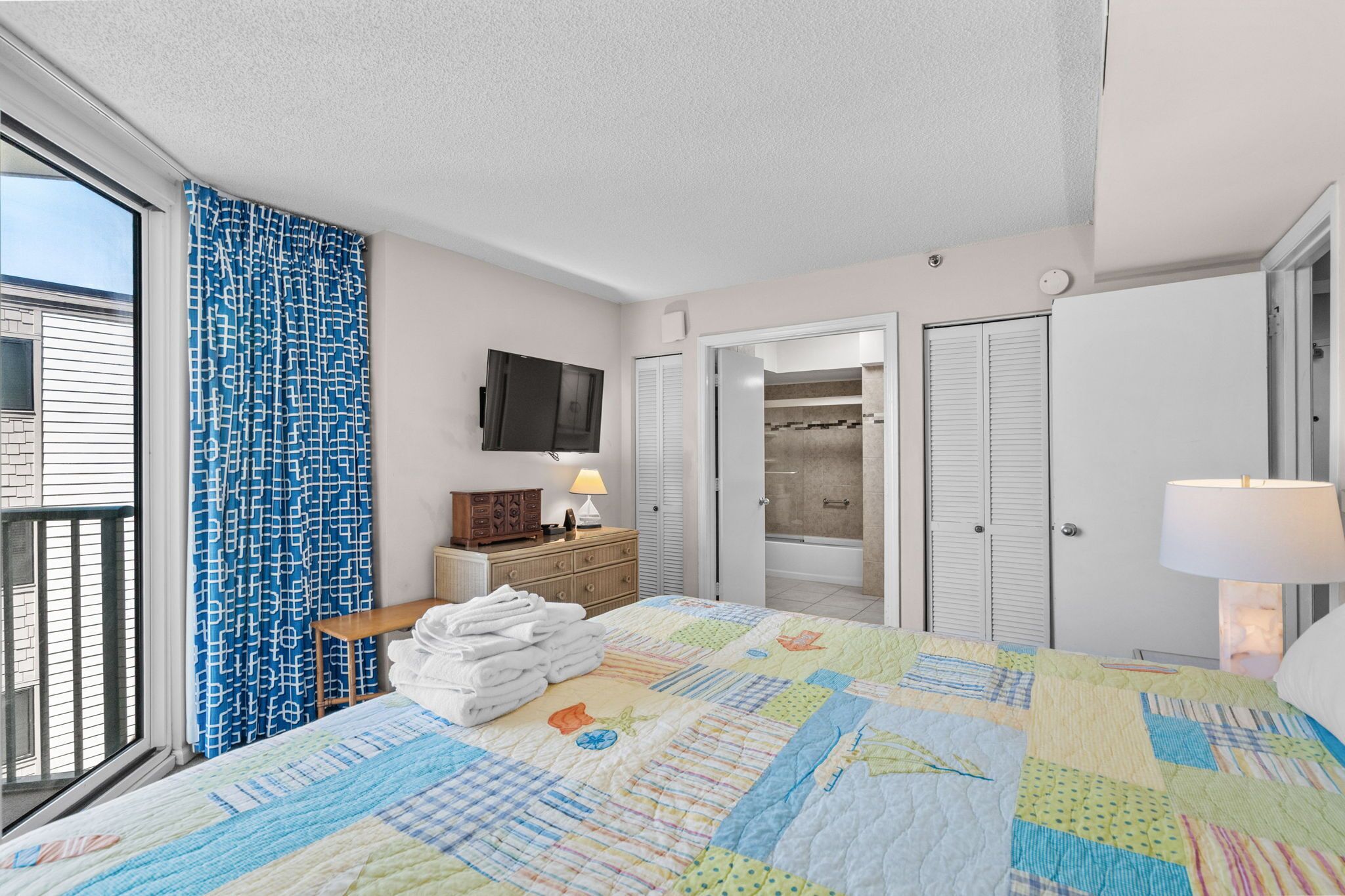 A hotel room with a bed, a TV, a bathroom with a shower, and a window with curtains.