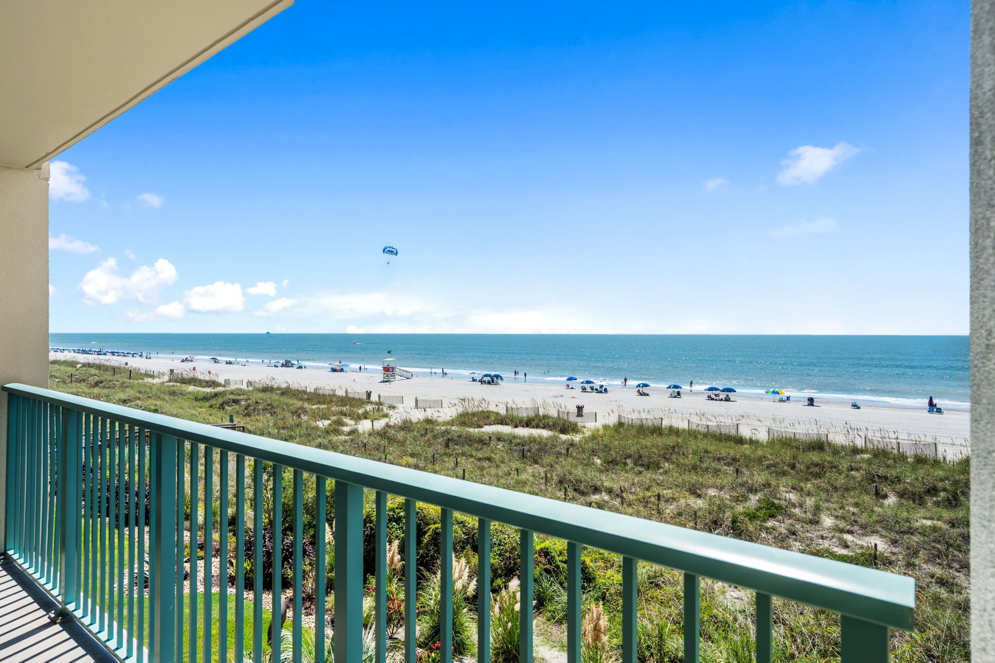 A beach view from a balcony with a railing, sandy beach, and ocean.