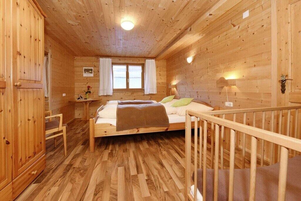 A wooden cabin bedroom with a bed, a desk, and a window.