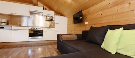 A modern kitchen with stainless steel appliances, a wooden ceiling, and a flat-screen TV mounted on the wall.