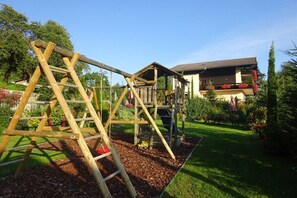 A wooden play structure in a garden with a house in the background. - Country House Bonaventura (Millstatt)