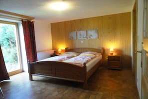 Ein Schlafzimmer mit einem hölzernen Bett, zwei Nachttischen mit Lampen, einem Fenster mit Vorhängen und einer Holzvertäfelung.