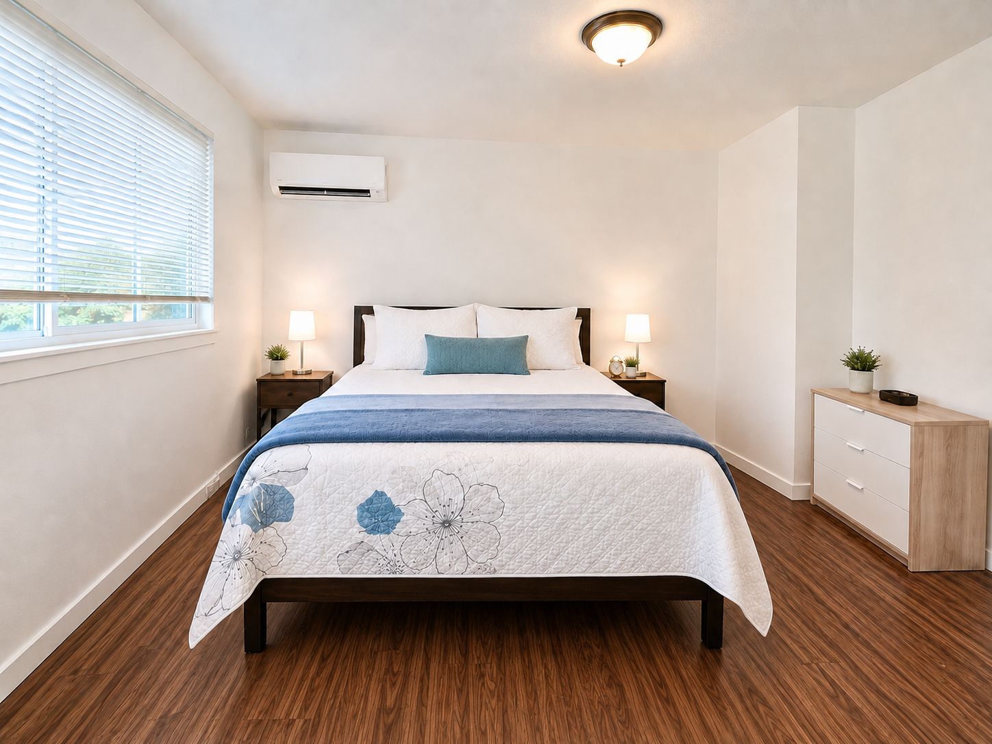 Ein Schlafzimmer mit einem Bett, Nachttischlampen, einem Nachttisch, einer kleinen Kommode und einer Klimaanlage.