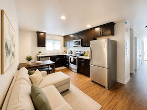 A modern kitchen with dark cabinetry, stainless steel appliances, and a dining area with a sofa and table. - 4b2b /AC /large deck/parking Queen Anne / Seattle (Seattle)