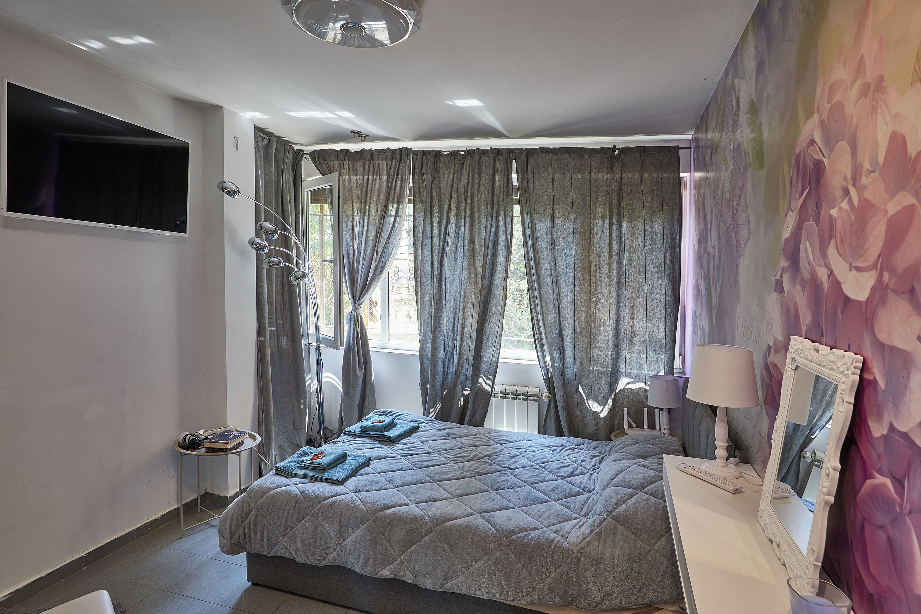 A bedroom with a bed, bedside tables, a mirror, and a window with curtains.