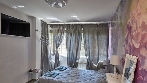 Un dormitorio con cama, mesitas de noche, un espejo y una ventana con cortinas.