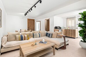 A modern living room with a sofa, coffee table, and a kitchen area in the background. - Aurelia Beach Residence by Nomads (Paphos)