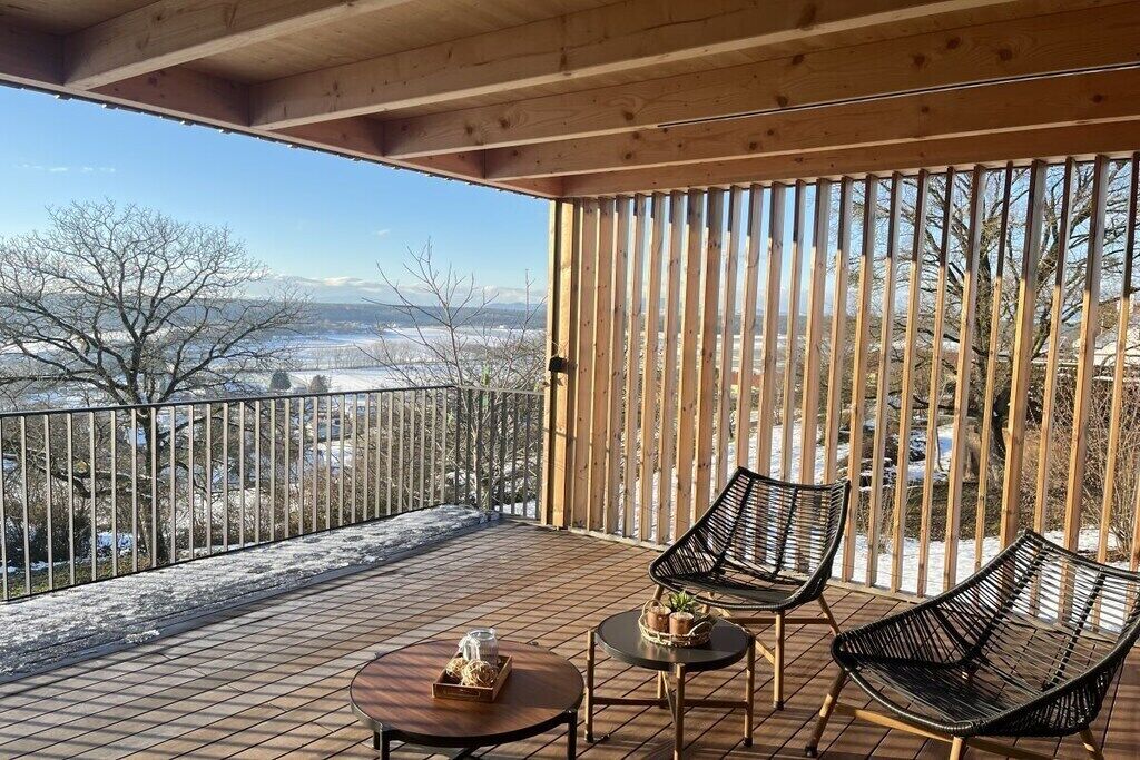 A wooden deck with two chairs and a table, overlooking a snowy landscape with mountains in the distance.