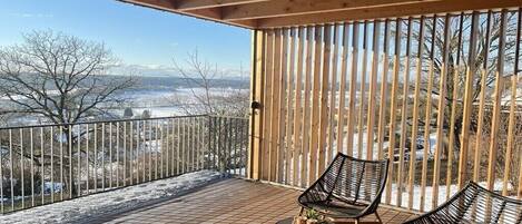 A wooden deck with two chairs and a table, overlooking a snowy landscape with mountains in the distance.