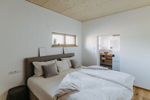 A bedroom with a bed, a window, a small kitchenette, and a trash bin. - Holiday home with 2 bedrooms (Litzelsdorf)