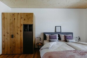 A bedroom with a wooden wardrobe, a bed with multiple pillows, and a small bedside table with a lamp. - Holiday home with 2 bedrooms (Litzelsdorf)