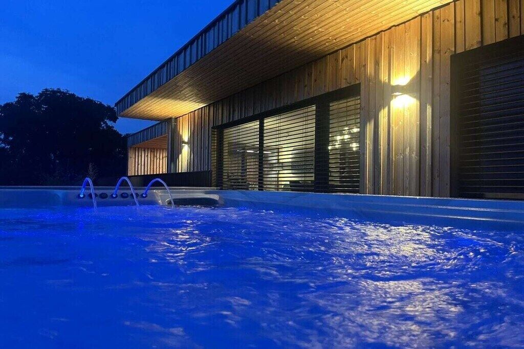 A swimming pool with a wooden deck and a modern building with large windows in the background.