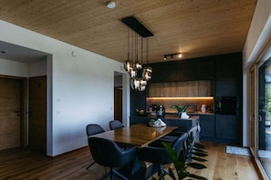 A modern interior with a wooden ceiling, a dining area with a wooden table and chairs, and a kitchen with dark cabinetry and a hanging light fixture. - Holiday home with 2 bedrooms (Litzelsdorf)