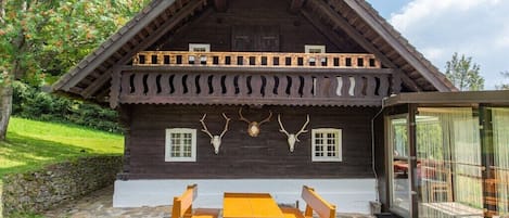 A wooden cabin with a balcony, a dining table, and benches.
