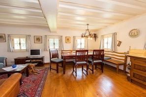 A spacious living room with wooden flooring, a dining table with chairs, a television, and a dog. - Holiday home in Anger with swimming pool (Anger)