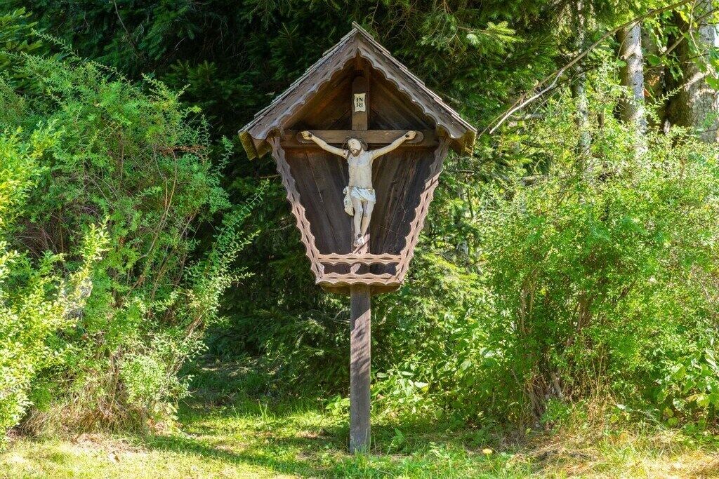 A wooden crucifix with a cross, surrounded by dense greenery.