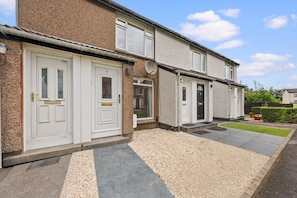A two-story residential building with a gravel driveway and a small garden area. - 2-bed Ground Floor Apartment with Free Parking Near Glasgow Airport (Renfrew)