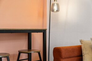 A room with a table and two stools, a hanging light fixture, and a cushioned seating area.